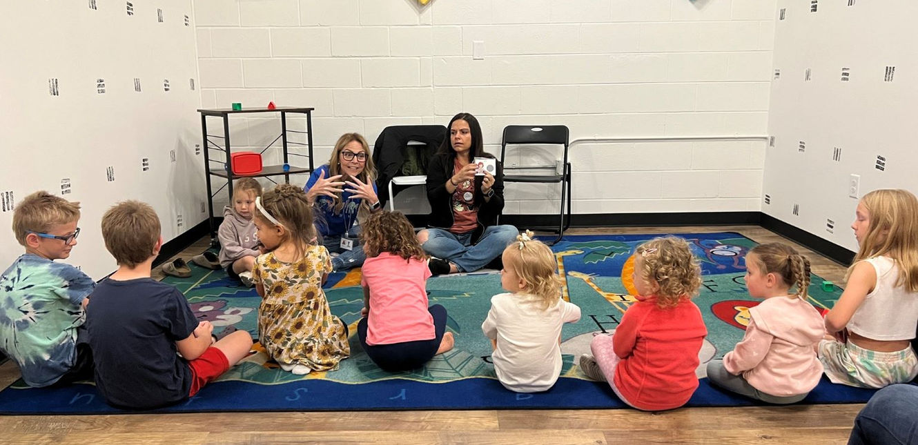2 teachers teaching 9 young children. All are sitting on the floor.