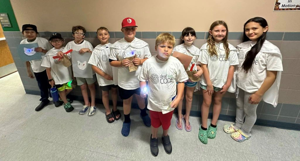 11 SDDeaf students standing in a hallway all are wearing white shirts.